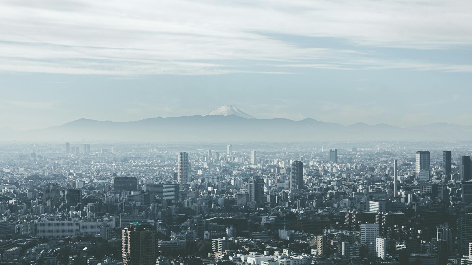 Panoramic view of Tokyo cityscape with Mount Fuji looming in the background, under cloudy skies.