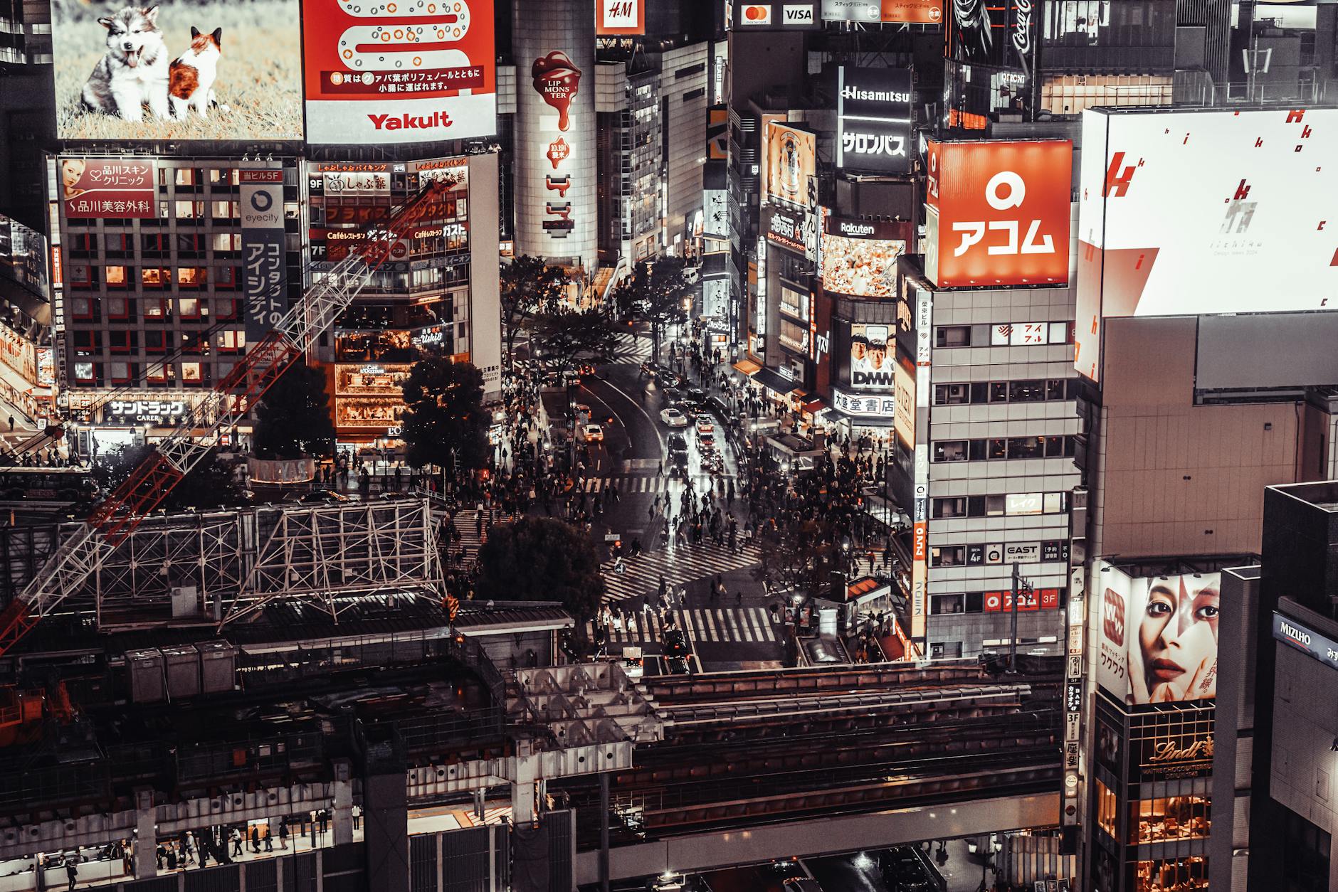 A bustling aerial view of Shibuya Crossing, Tokyo at night, showcasing vibrant city life and illuminated billboards.