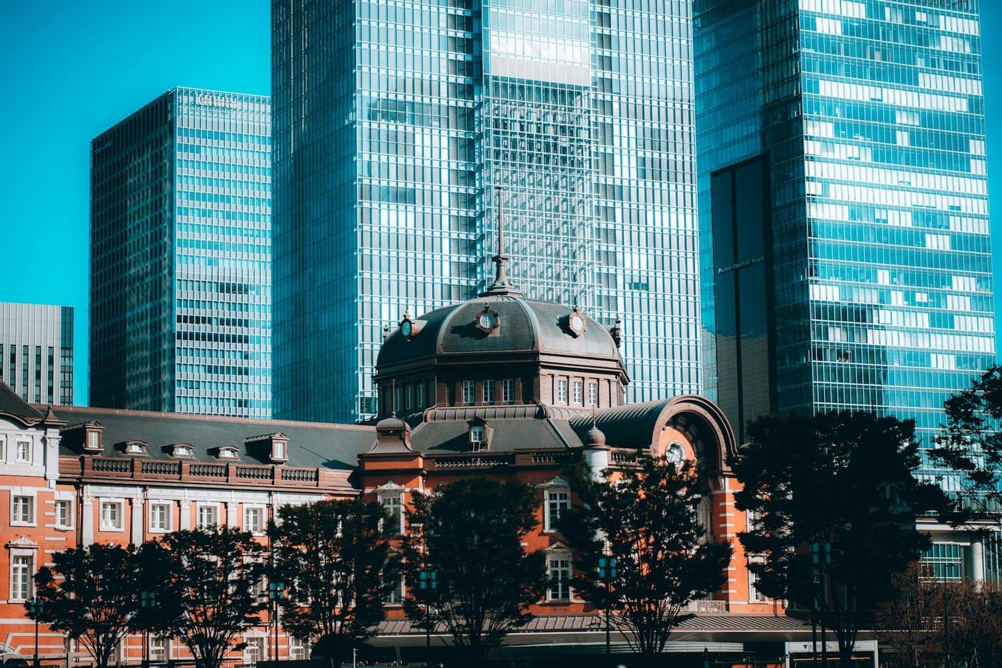 Urban scene of modern skyscrapers and historic Tokyo Station in vibrant morning light.