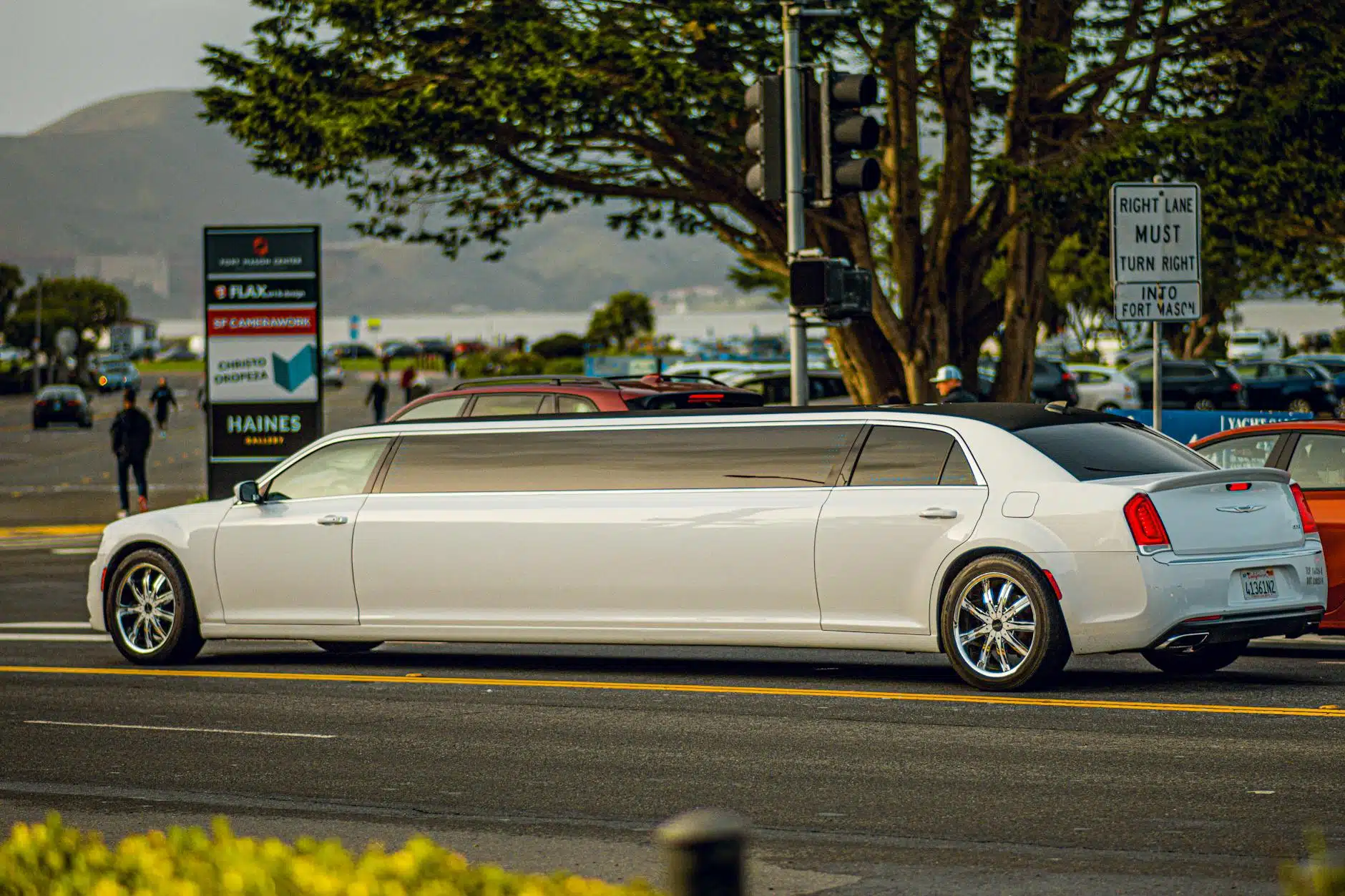 A white limousine driving on a street in San Francisco with a scenic background.