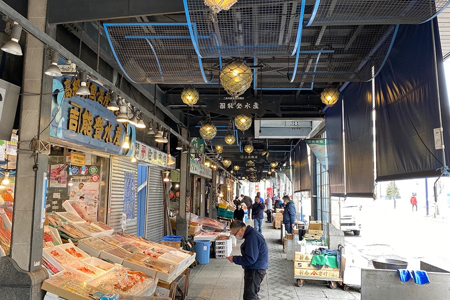 札幌二條市場的拱廊通道，兩側鮮魚店擺滿冰鎮海產，頭上掛著玻璃浮球燈飾