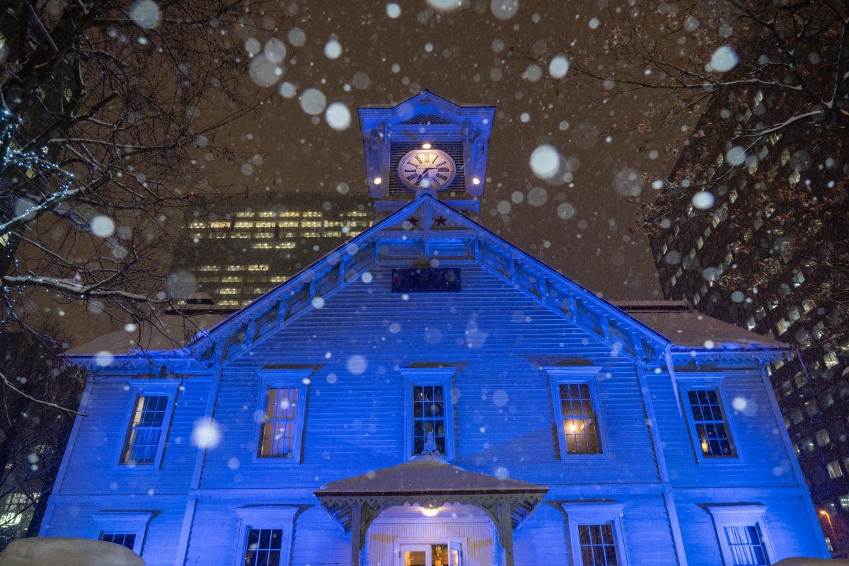 雪夜中亮起藍色燈光的札幌市時計台木造鐘樓外觀
