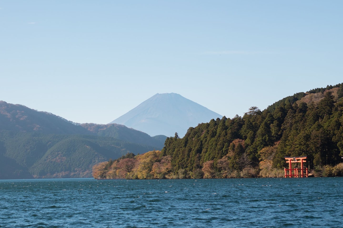 Picturesque view of Mount Fuji and red torii gate with lush greenery by Lake Ashi, Japan.