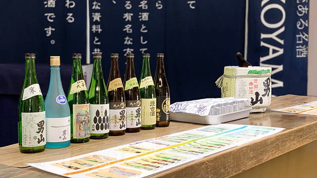 男山酒造資料館的試飲販售區櫃檯，排列多款男山清酒酒瓶與菰樽