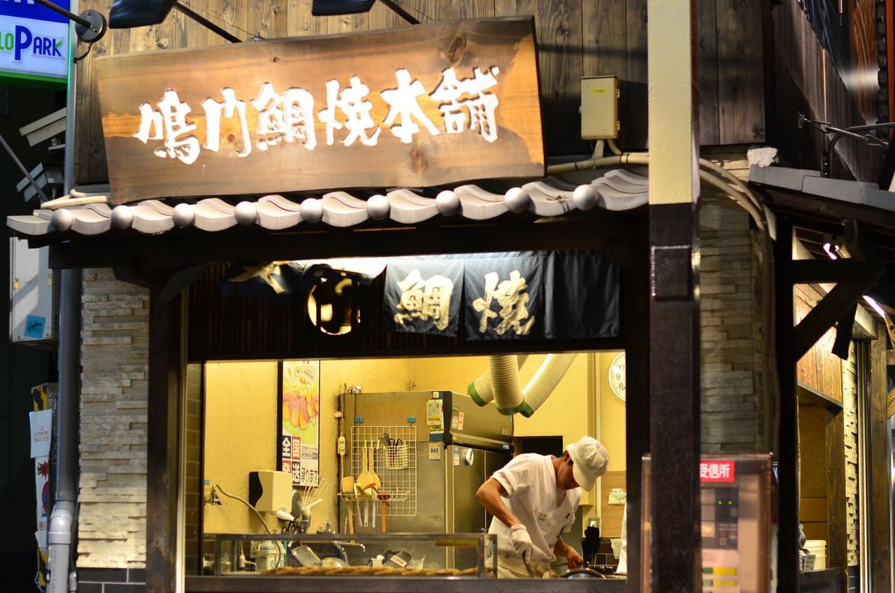 Chef preparing delicious Japanese street food at night in Osaka's vibrant Dotonbori.