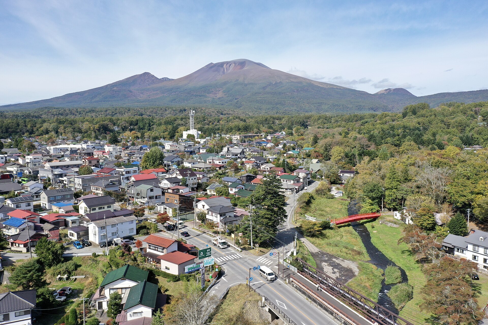 Aerial view of Karuizawa town with rooftops, a red bridge over a stream, and a volcano behind