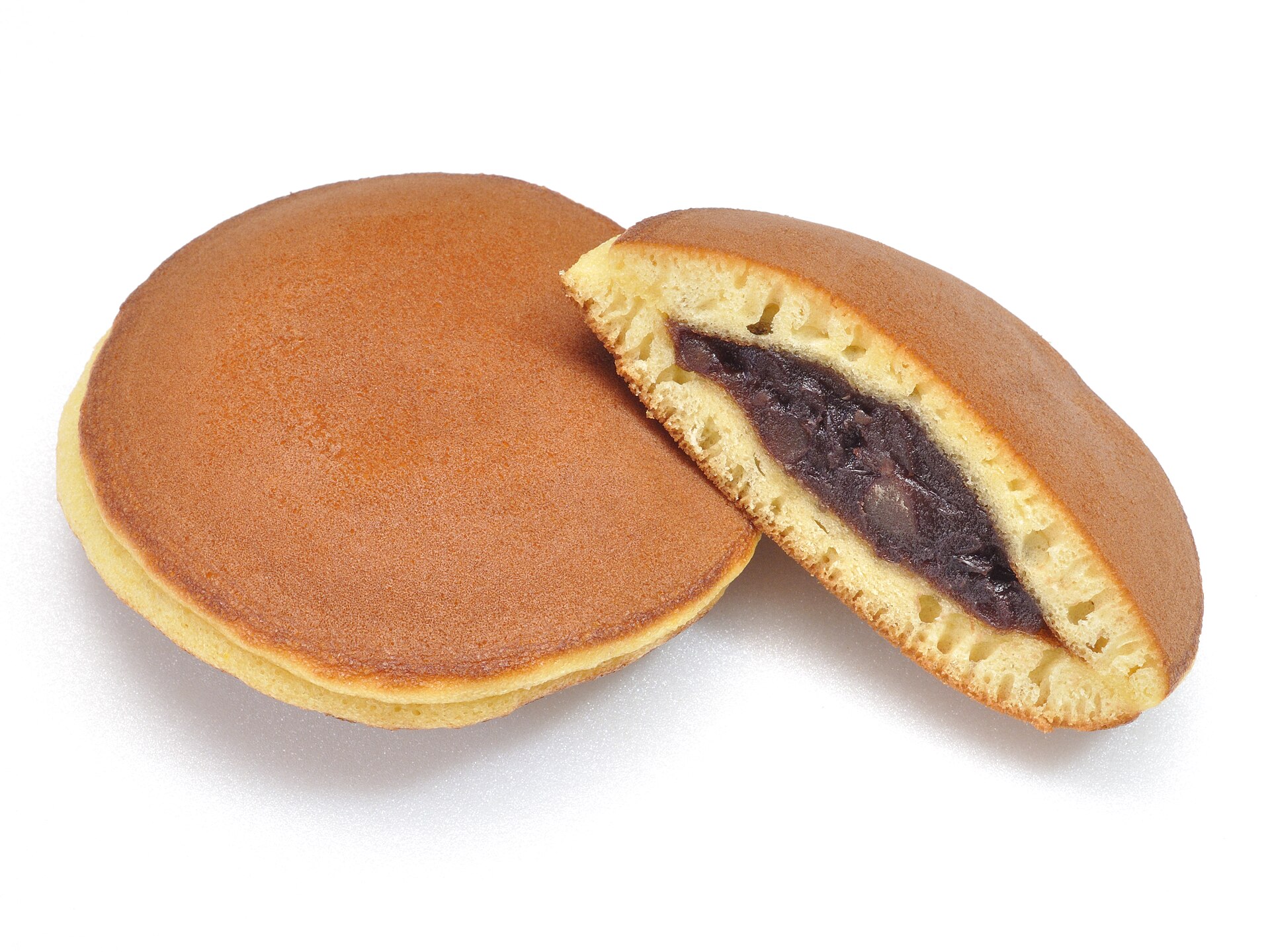 Two dorayaki on a white background, one halved to show red bean paste filling