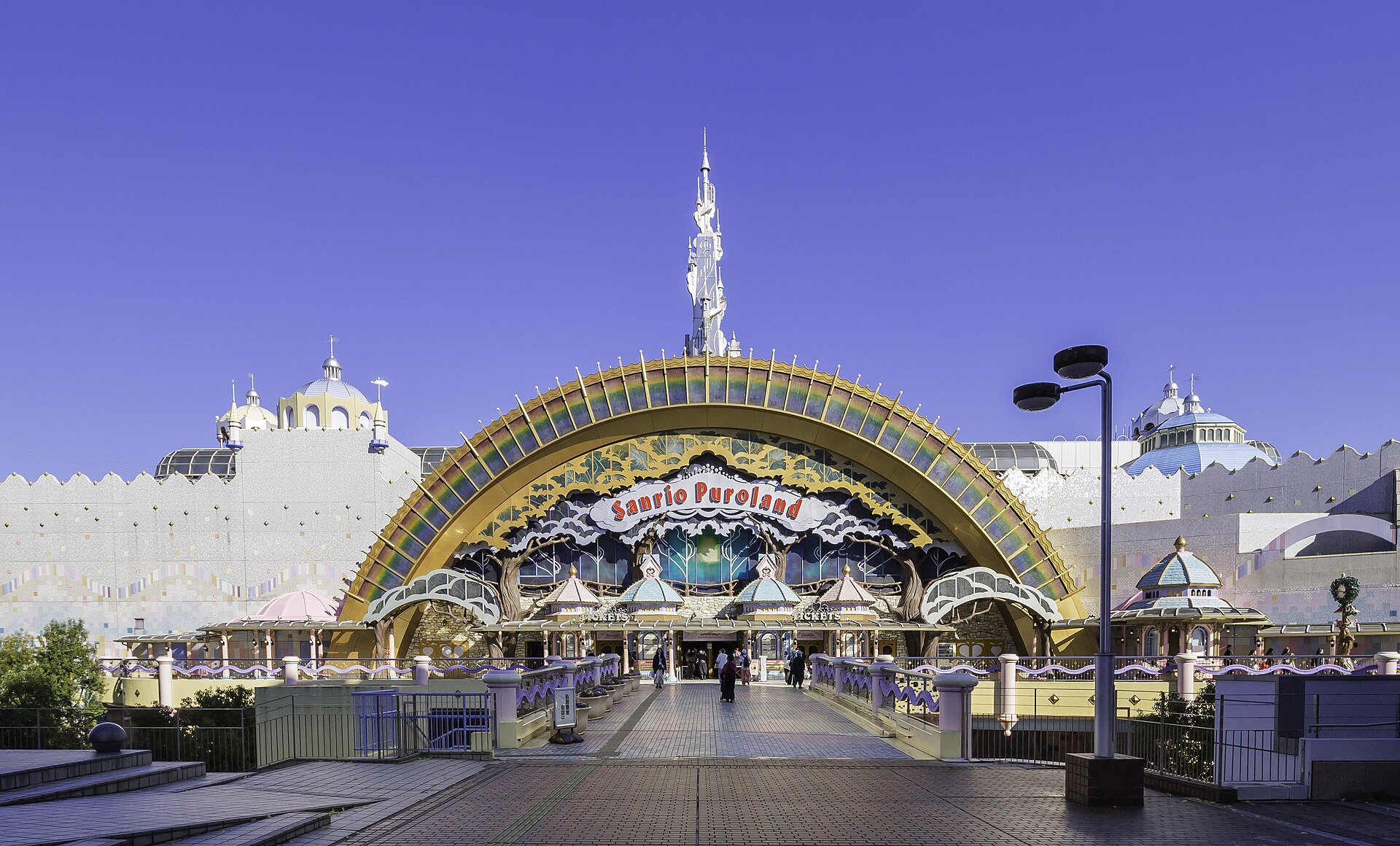 Entrance of Sanrio Puroland with a gold rainbow-arched gate reading 'Sanrio Puroland' under a clear blue sky.