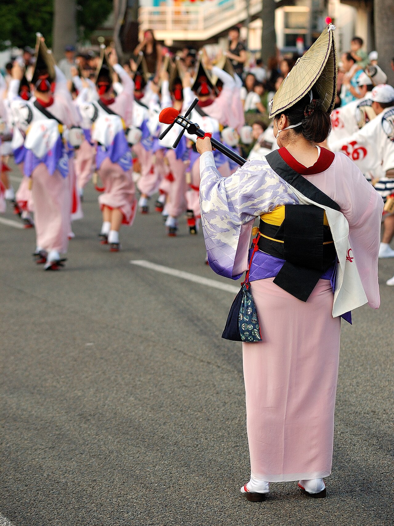 ピンクの着物と編笠姿の女踊りの踊り手が、通りを列になって踊っている様子