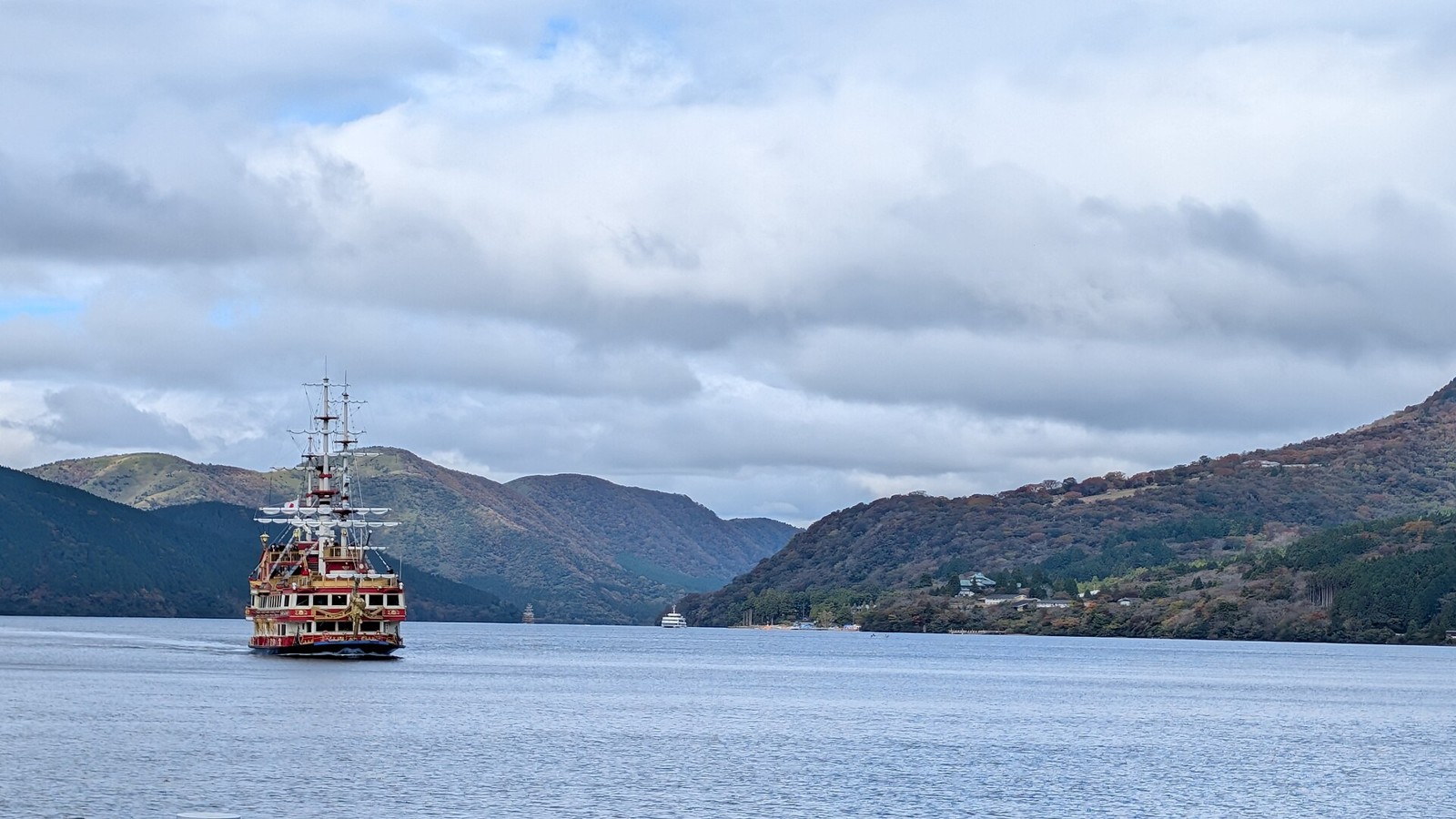 A red-and-gold pirate-style ship sailing on Lake Ashi, with forested hills under cloudy skies
