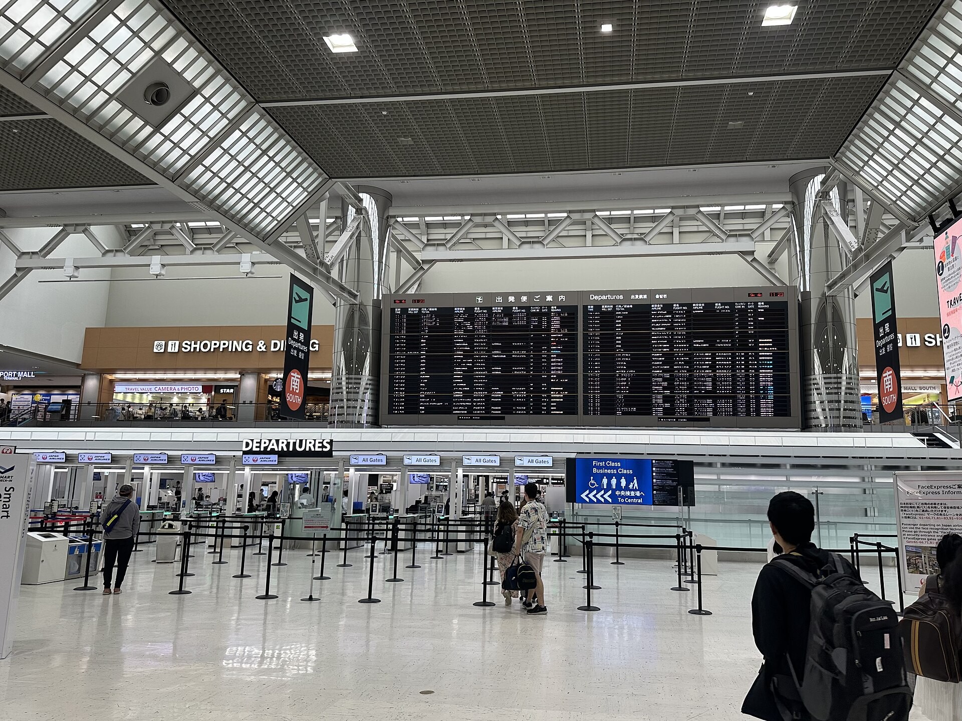 Narita Airport departures hall with a large flight information board above check-in counters and travelers with luggage