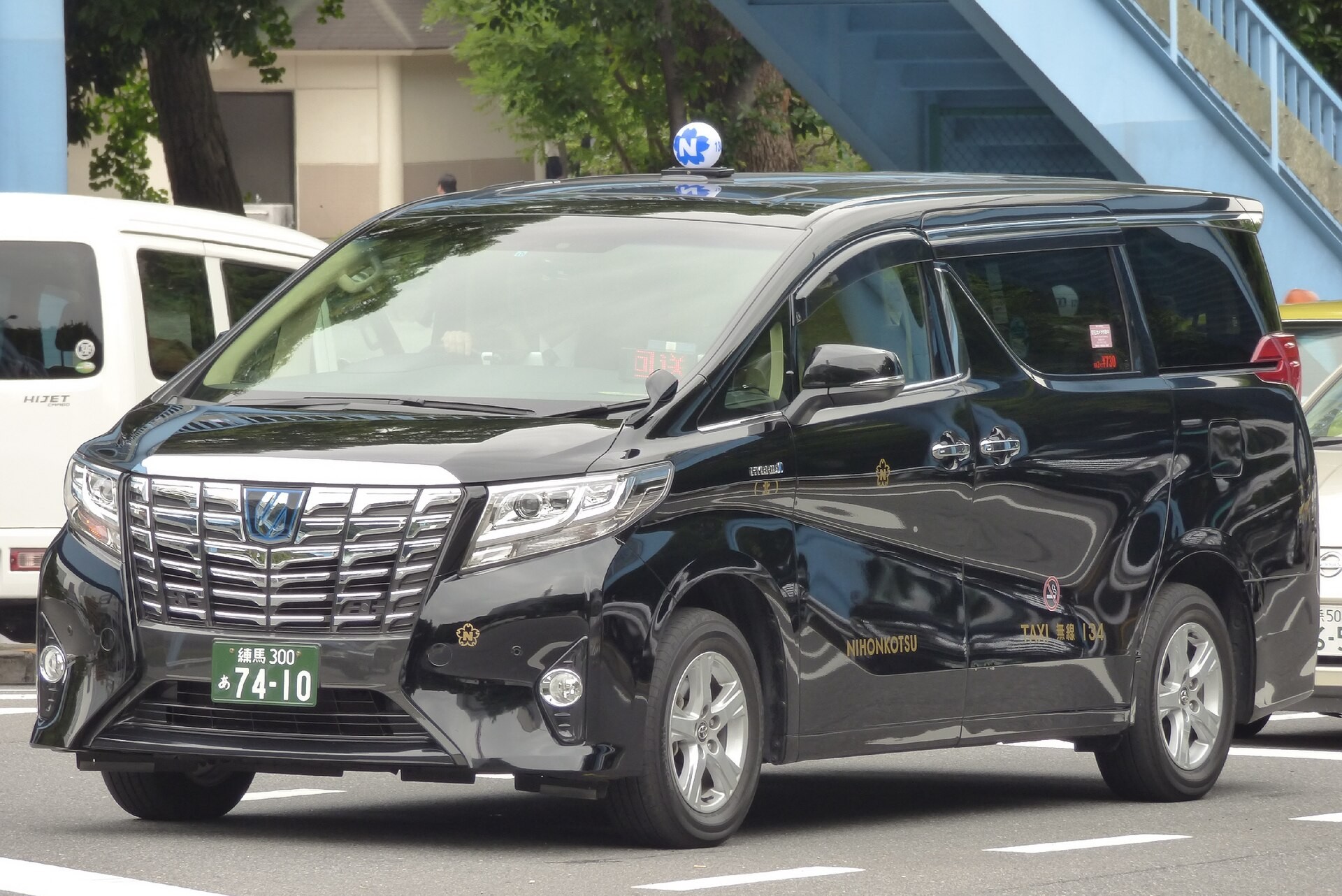 A black Toyota Alphard minivan taxi with NIHONKOTSU and TAXI markings on a city street