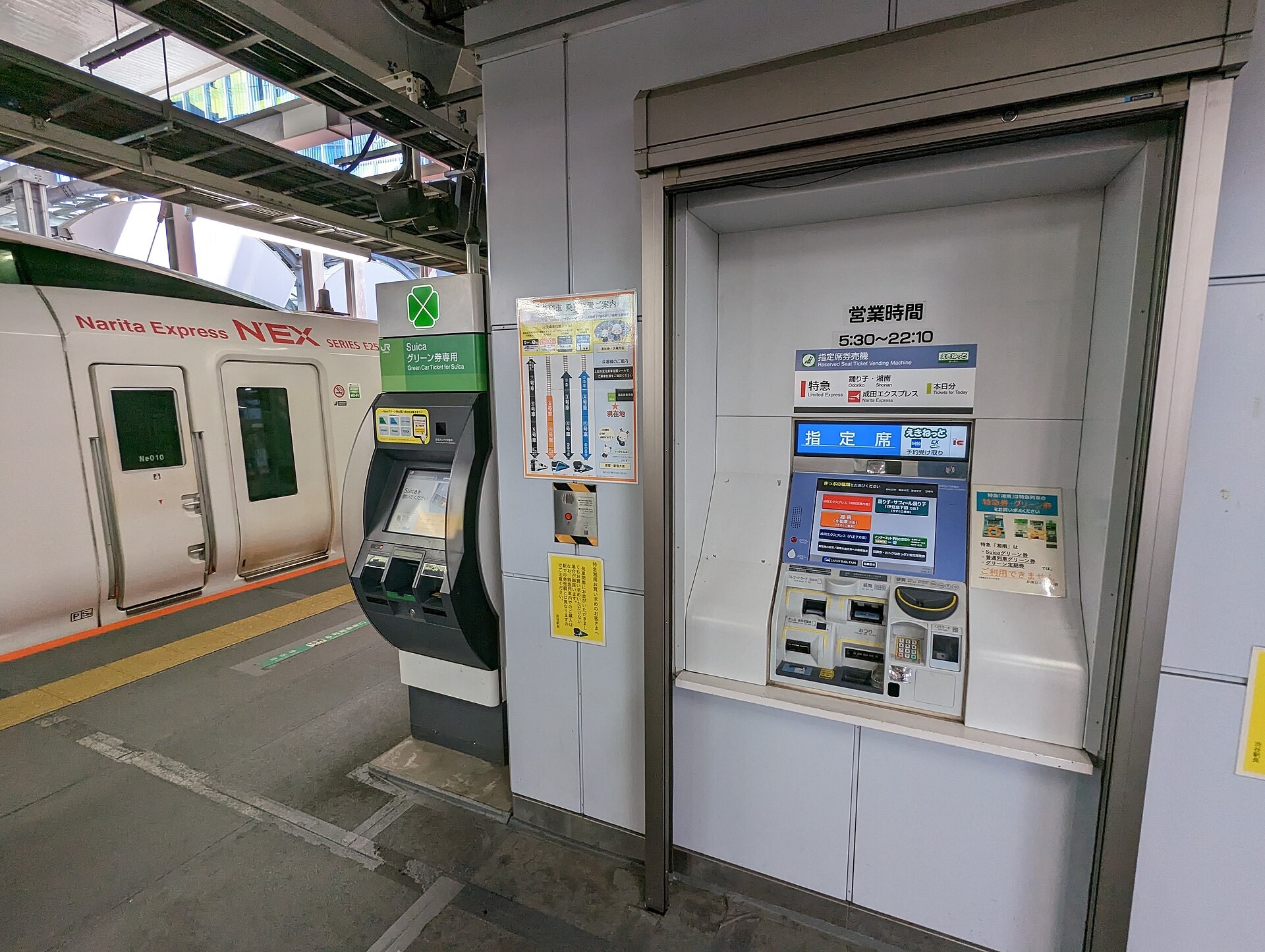 Reserved-seat ticket vending machine and Suica Green Car ticket machine on a platform beside a Narita Express NEX train.