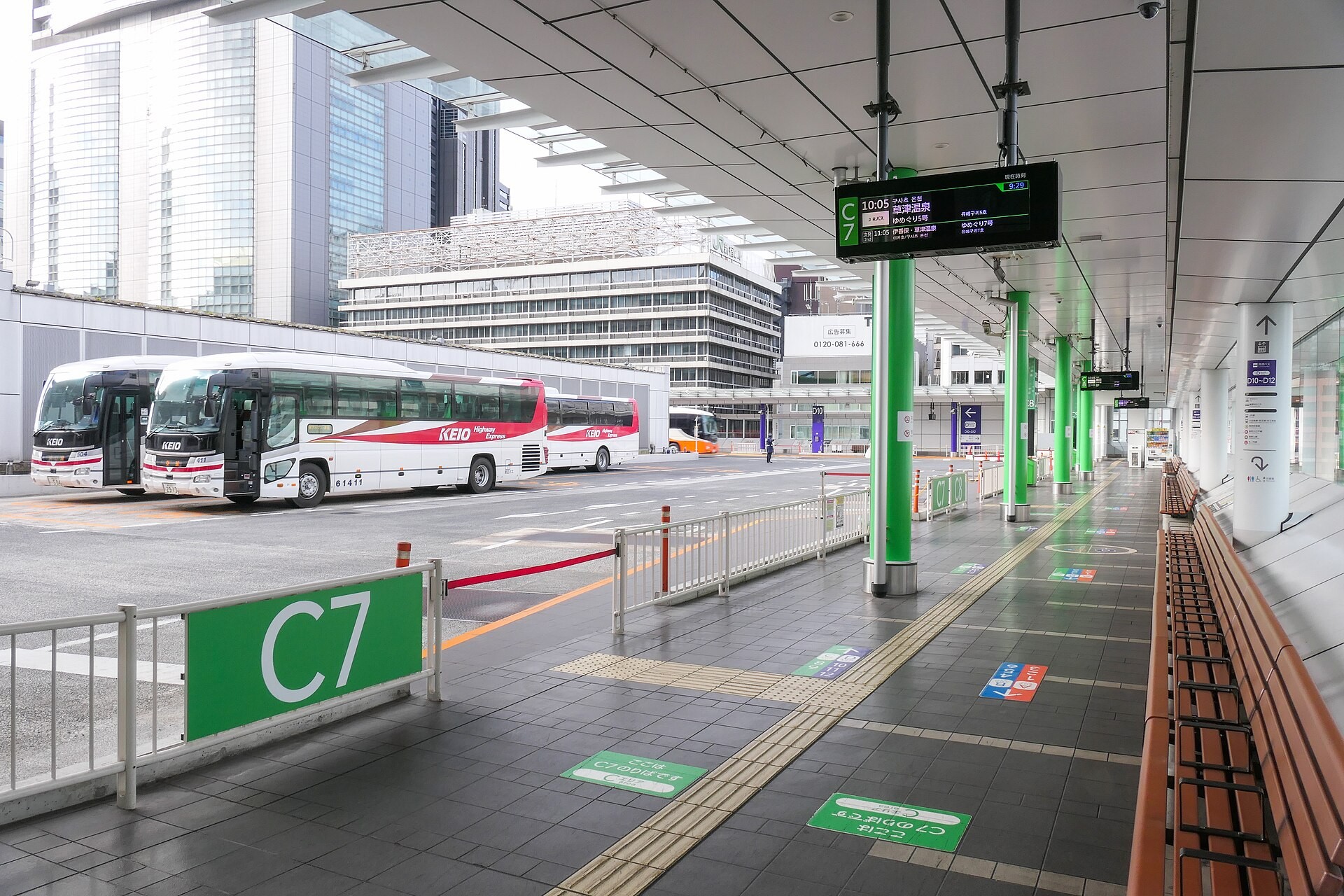 Bus terminal platform with white-and-red long-distance coaches parked beside a green C7 stop sign and benches.