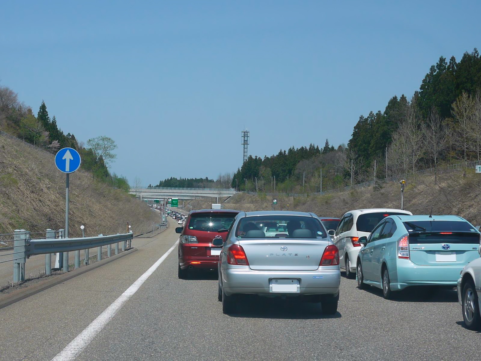 Heavy traffic jam on a highway with cars queued in lanes, trees and a bridge ahead