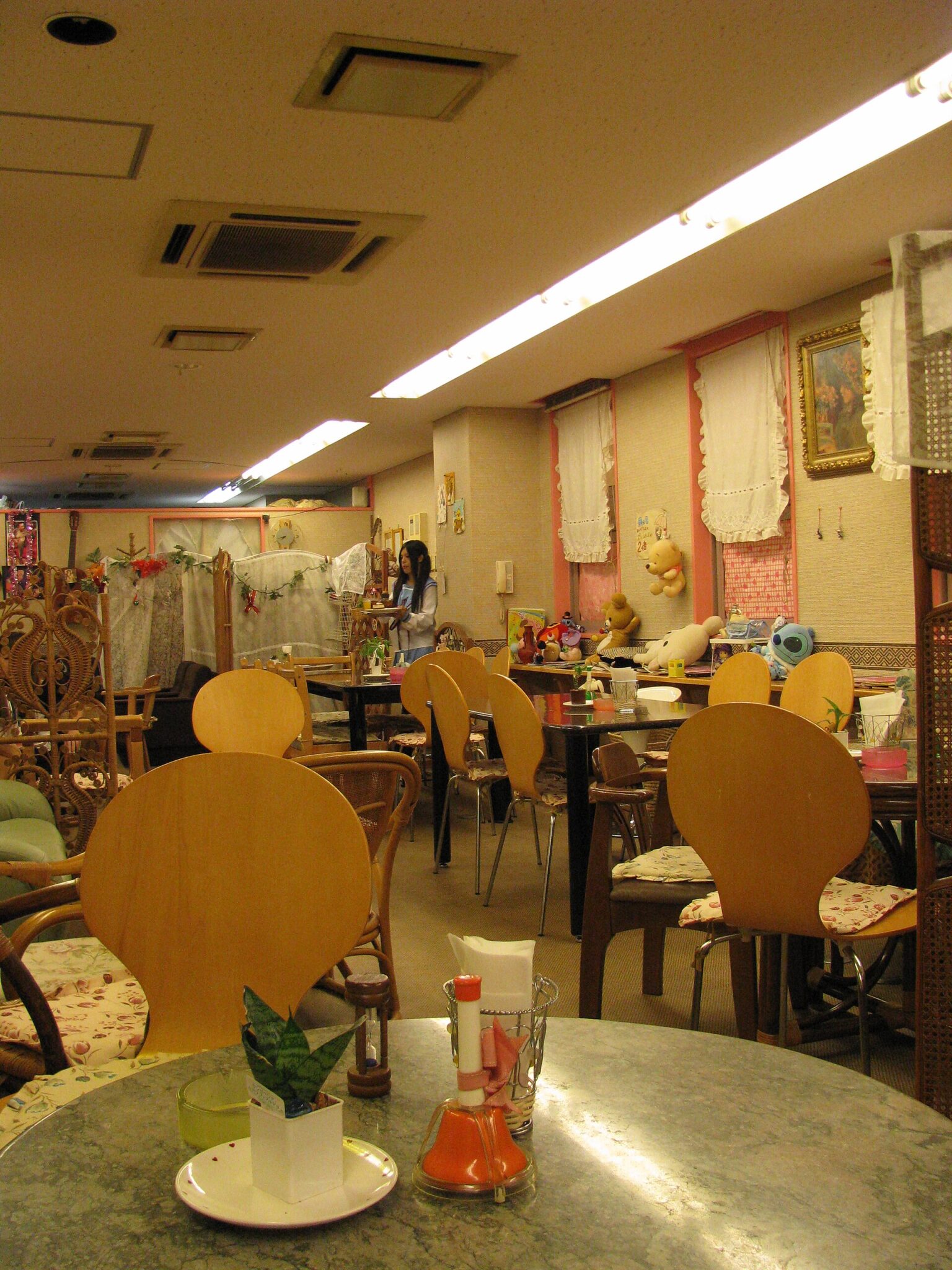 Interior of a cafe with round tables, wooden chairs, plush toys, and lace curtains.