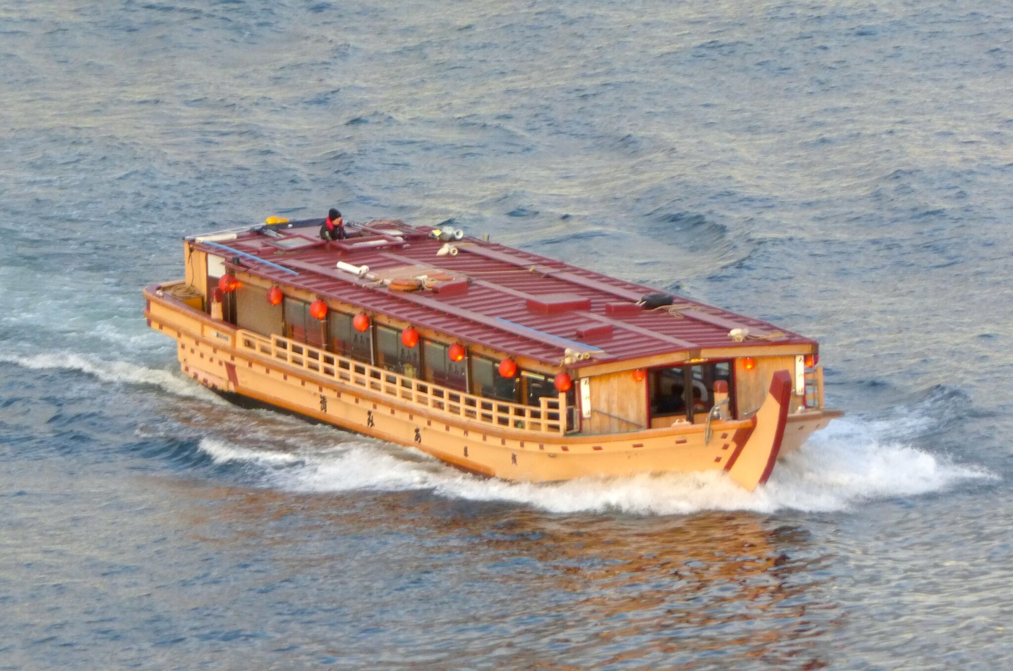 A wooden red-roofed yakata boat with red lanterns cruises across choppy water