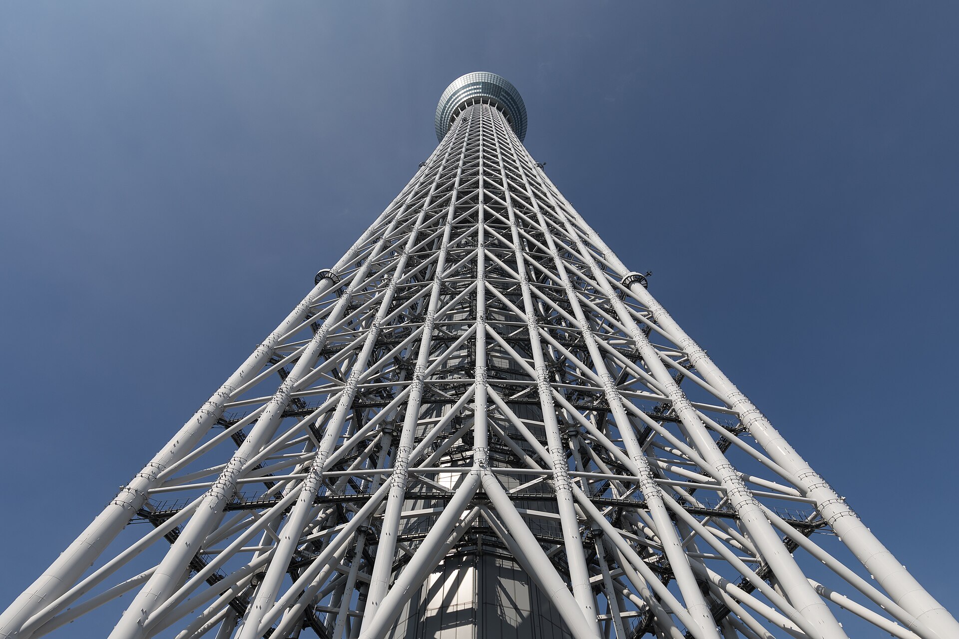 Low-angle view of the white steel lattice frame of Tokyo Skytree tapering up to its observation deck against a deep blue sky