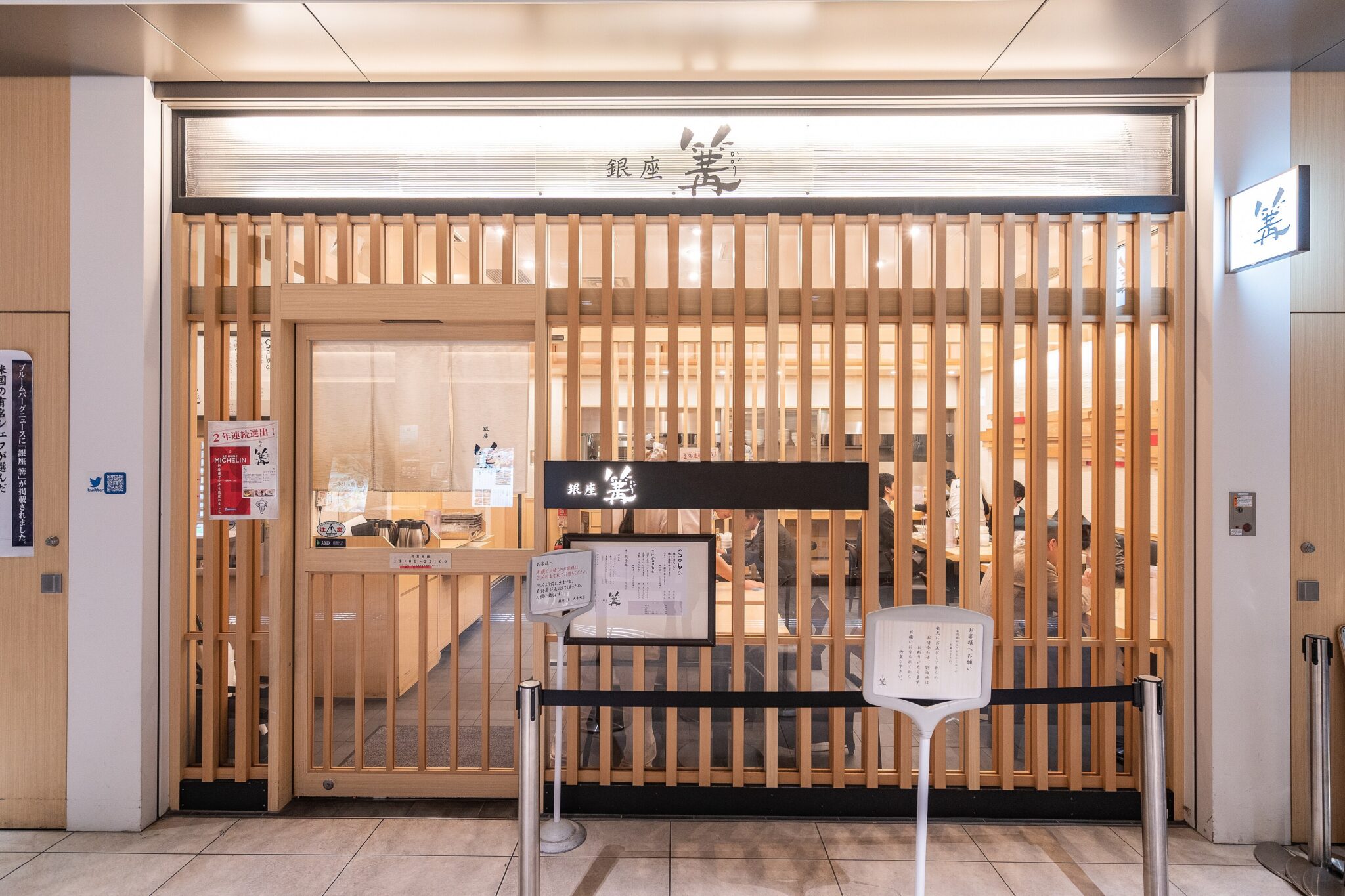 Wooden slatted storefront of the Ginza ramen restaurant Kagari, with entrance signage and queue barriers