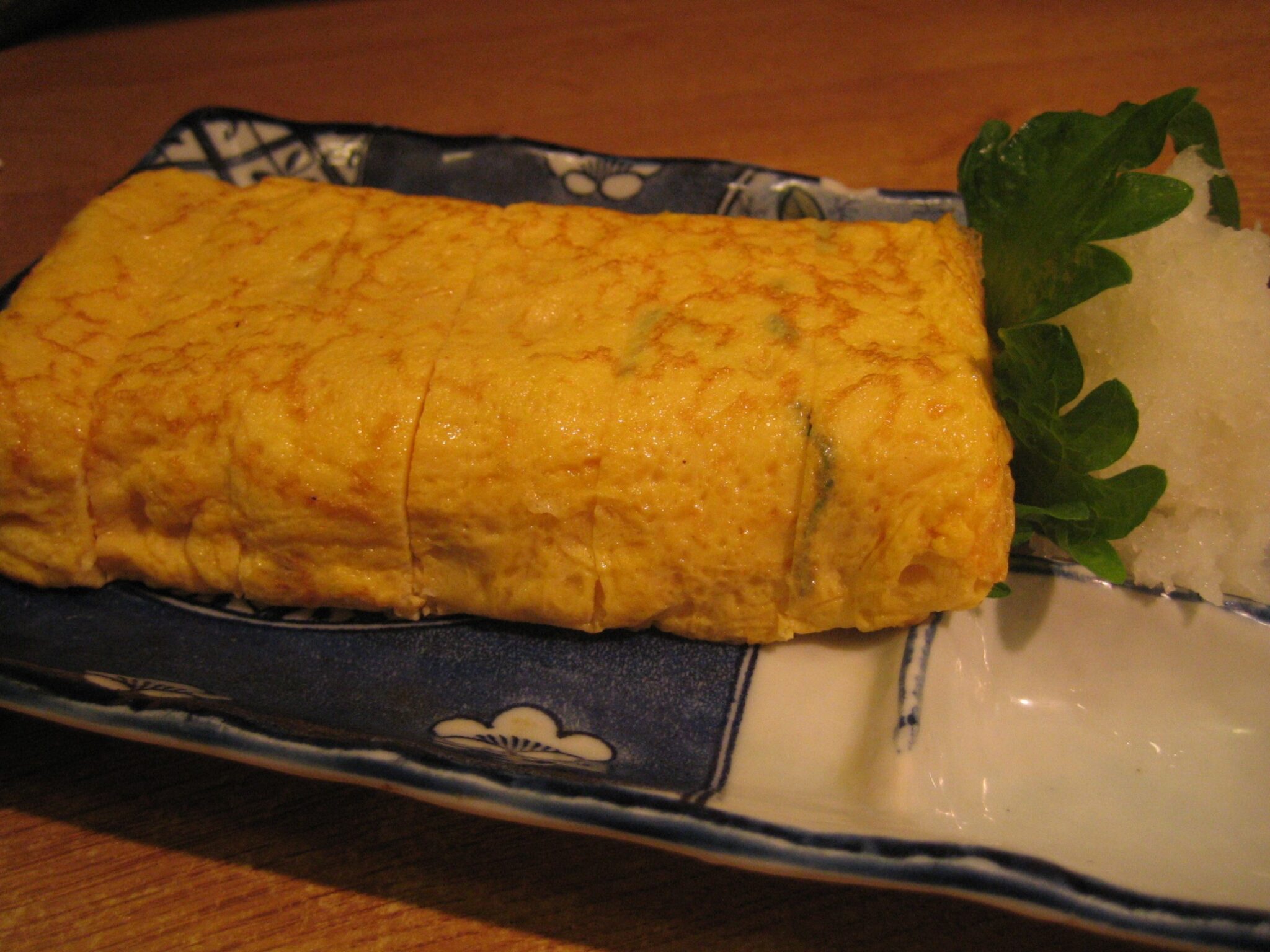 青と白の模様の長皿に盛られた厚焼き卵焼き。大根おろしと青菜を添えて