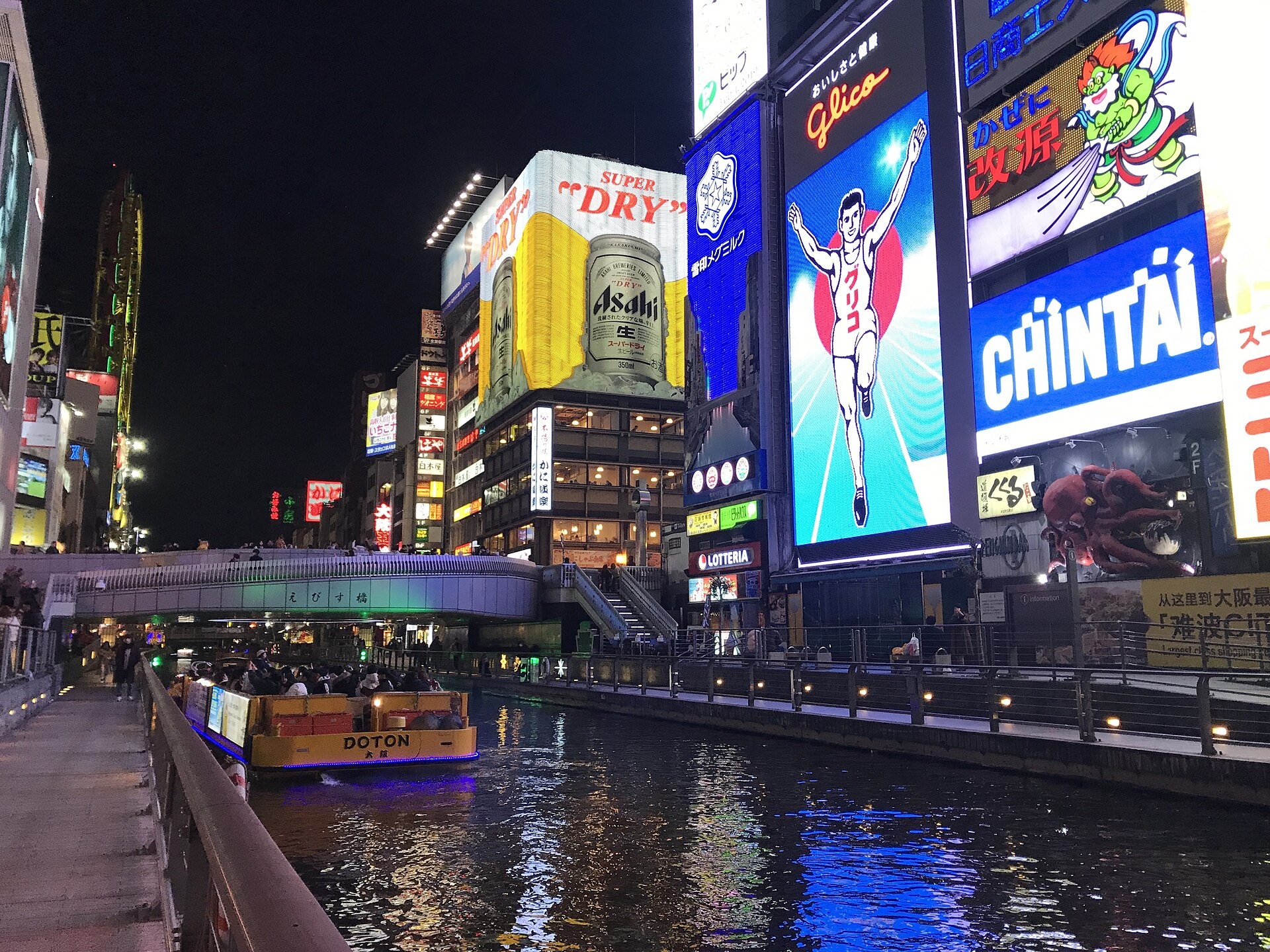 Dotonbori canal at night with the Glico runner billboard and a yellow tour boat