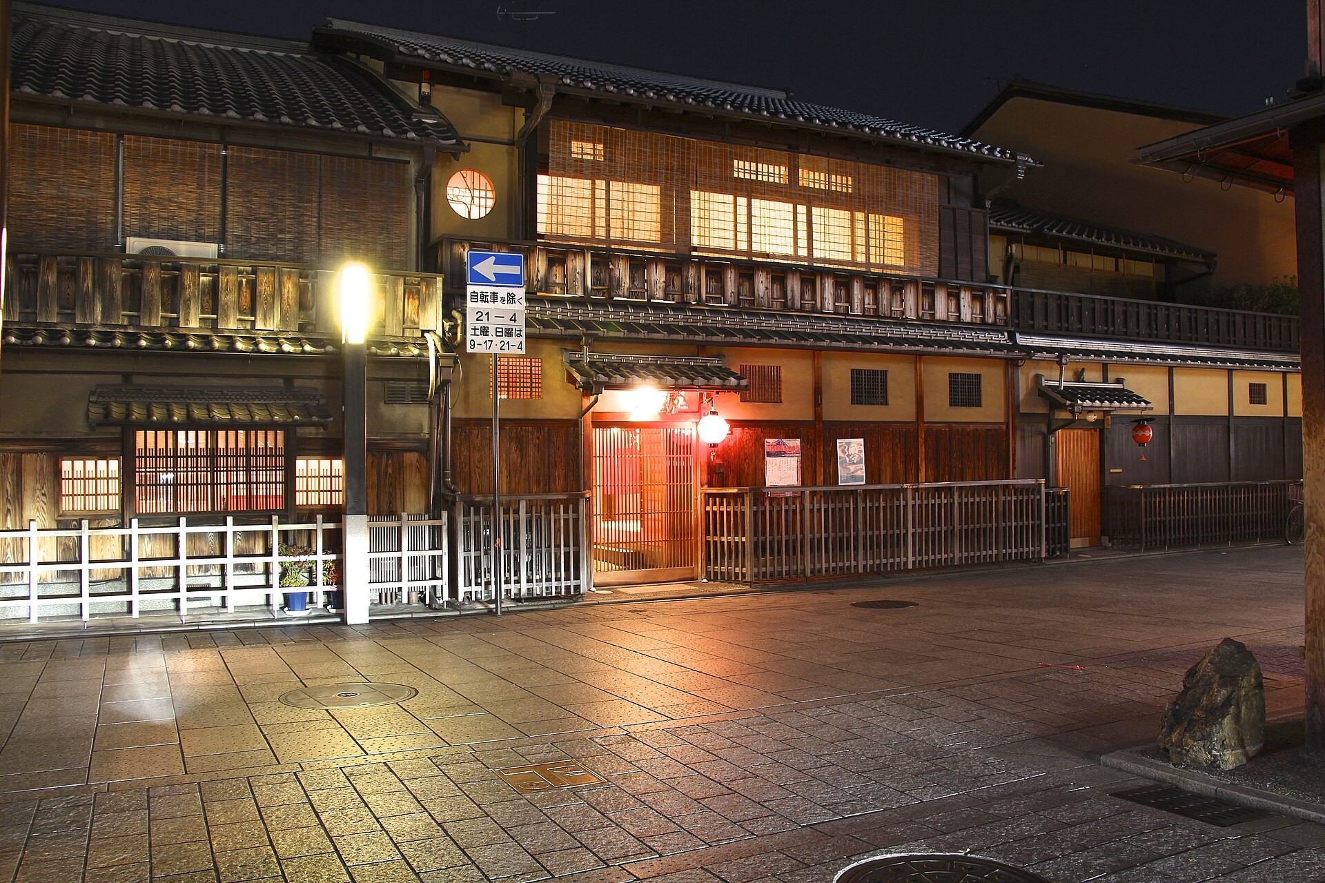 Traditional wooden machiya townhouses with lit red lanterns on a nighttime Kyoto street