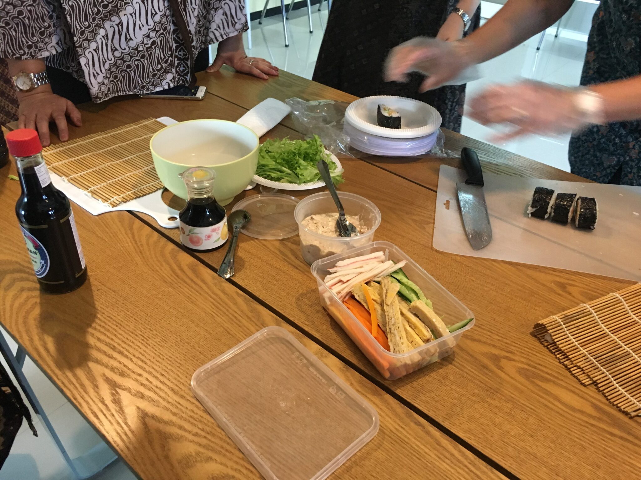 Wooden table with sushi ingredients, bamboo mats, and sliced nori rolls