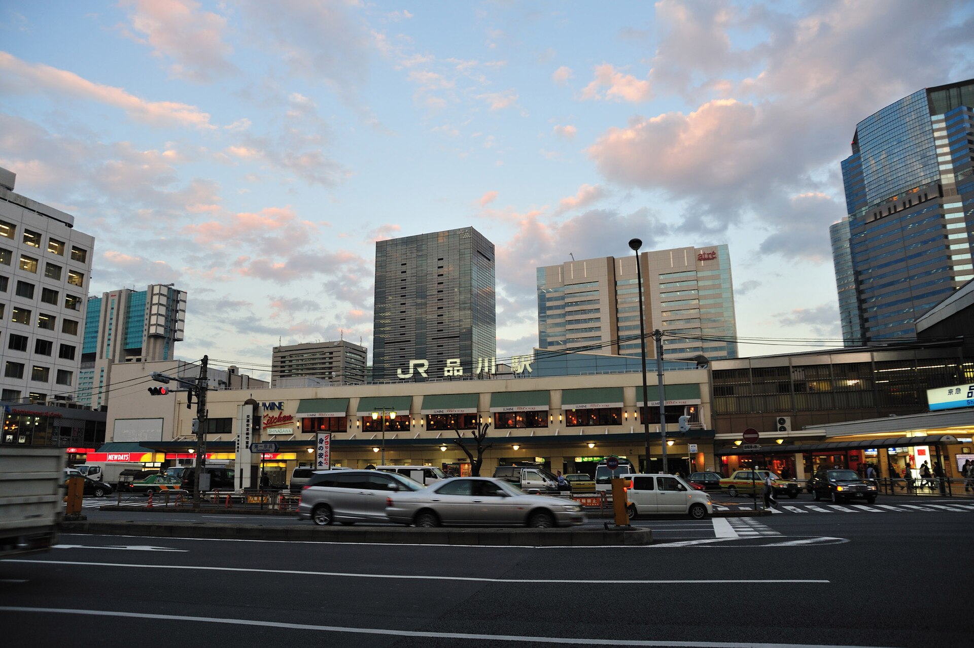 Shinagawa Station facade at dusk, with cars on the road and tall buildings behind